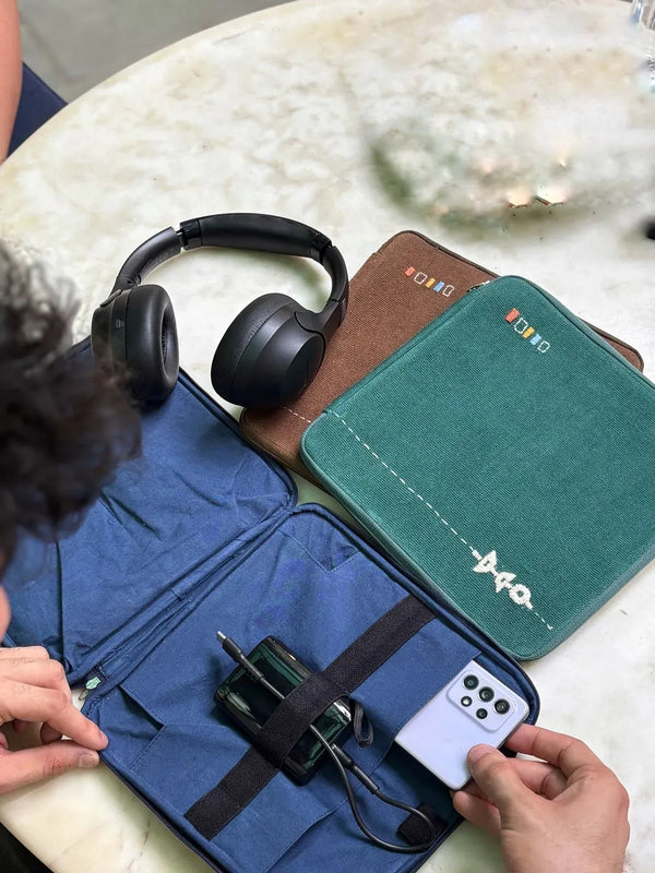 Green hand-embroidered gadget bag holding a charger, cable and earphone case on a desk