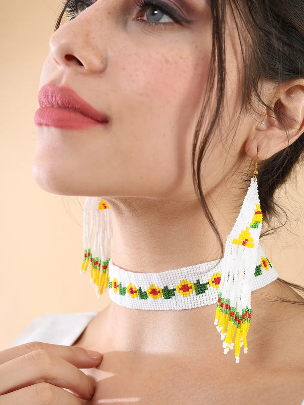 Woman wearing a white glass bead choker with yellow flowers and green leaves, and long white fringe earrings
