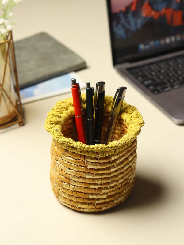 Handwoven wheat grass pen holder in warm straw tone standing on a wooden office desk
